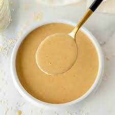 tahini poured from a spoon into a small bowl on a wooden table